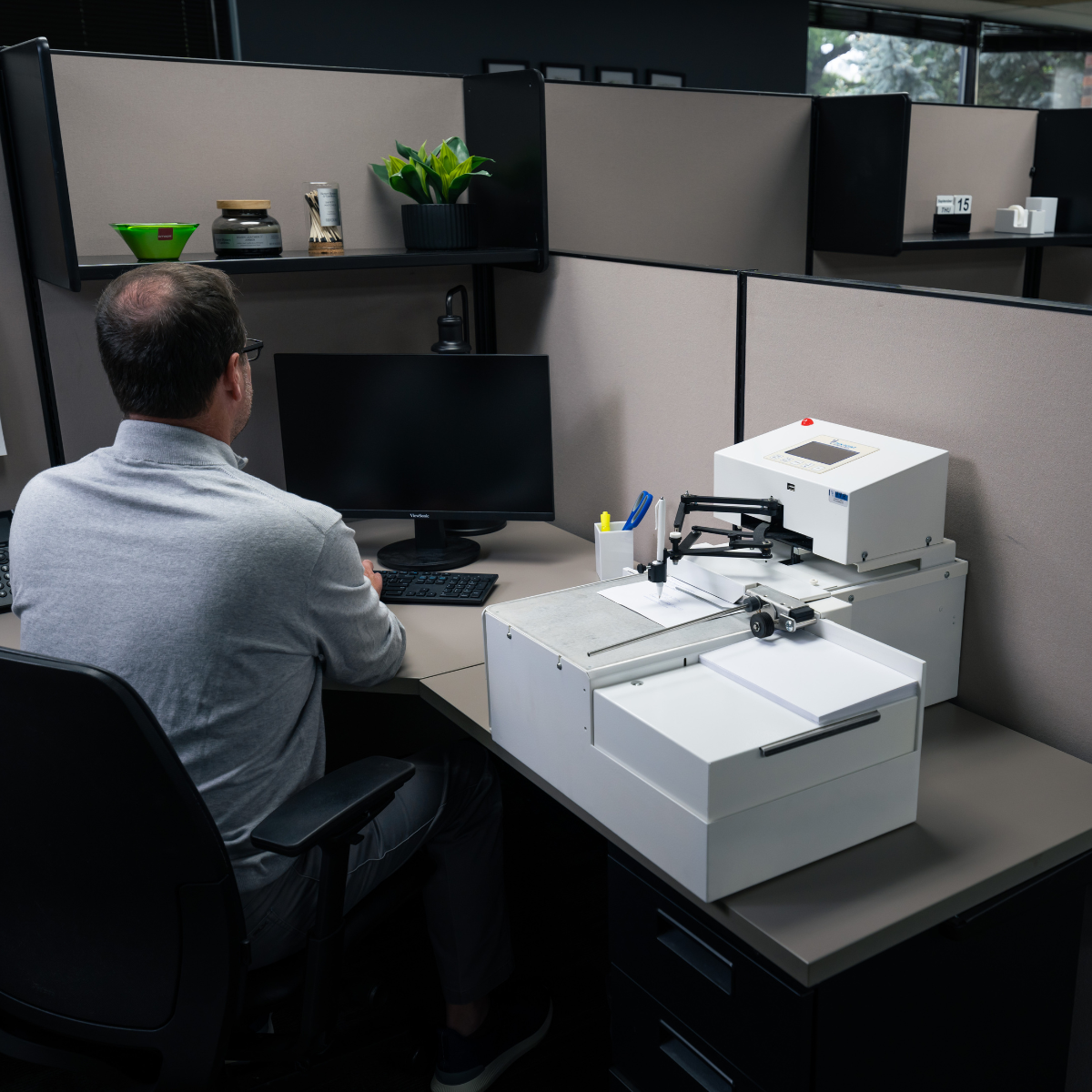 An employee starting a job on a UniProd handwriting machine from his desk in a normal office cubicle