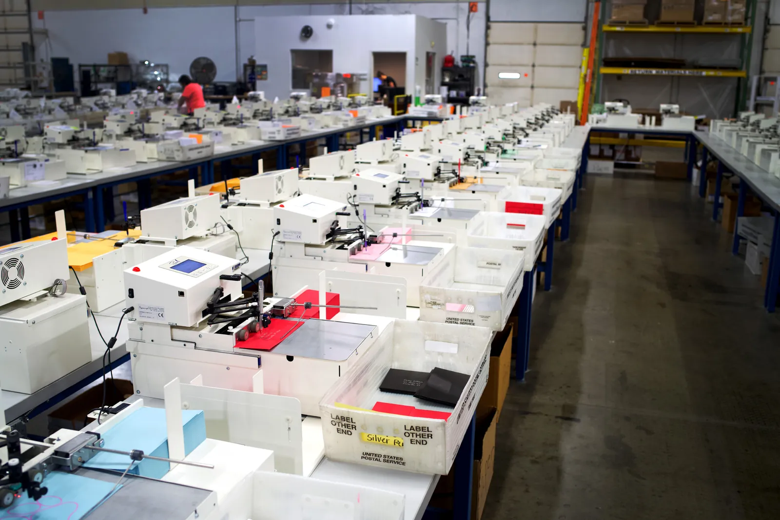 Rows of UniProd handwriting machines writing envelopes into postal trays on a production floor