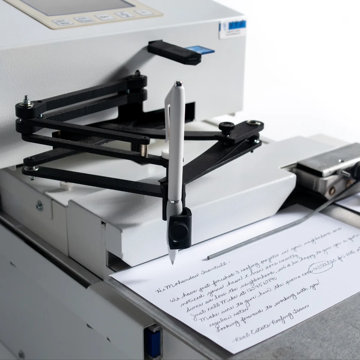 The UniProd's arm holding an ordinary pen over a handwritten letter in the writing bed