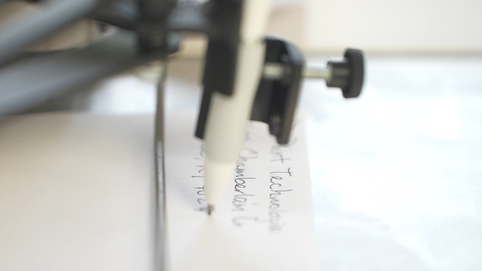 Close-up of a UniProd handwriting machine's ballpoint pen writing on an envelope